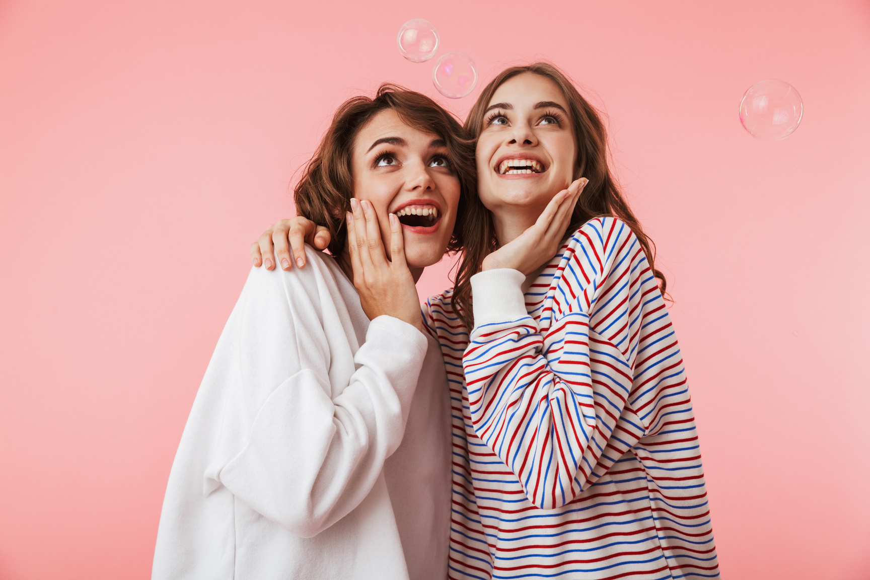 Happy Women Friends Isolated over Pink Wall Background over Soap Bubbles.